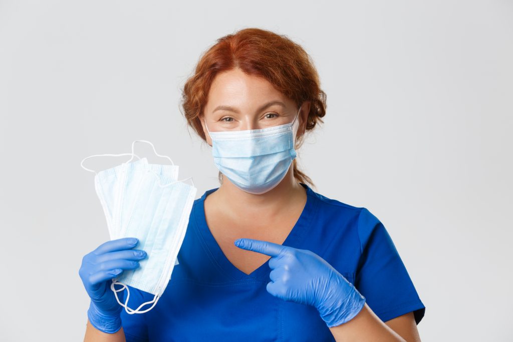 Medical workers, covid 19 pandemic, coronavirus concept. Close up of smiling caring female nurse, doctor in rubber gloves pointing at face masks, ask social distancing, explain main recommendations